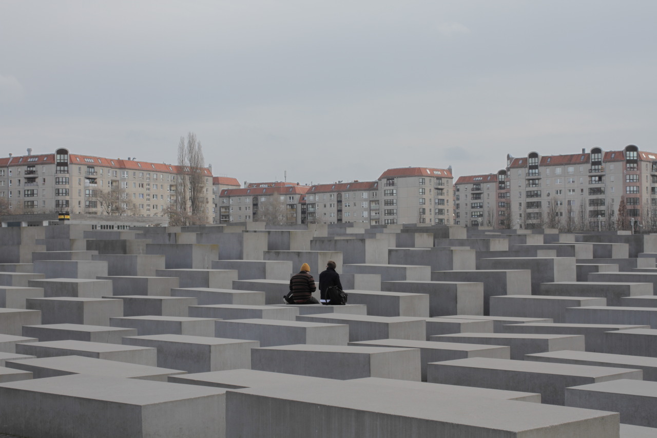 A desaturated photograph of two people sitting among concrete blocks.