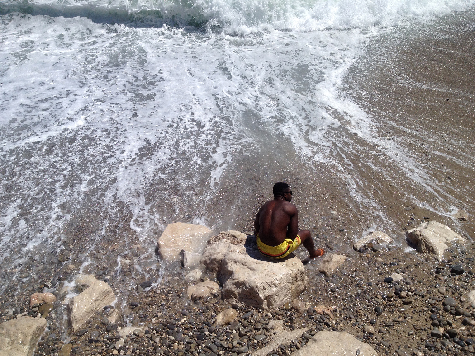 A color photograph of a man sitting at the shoreline.