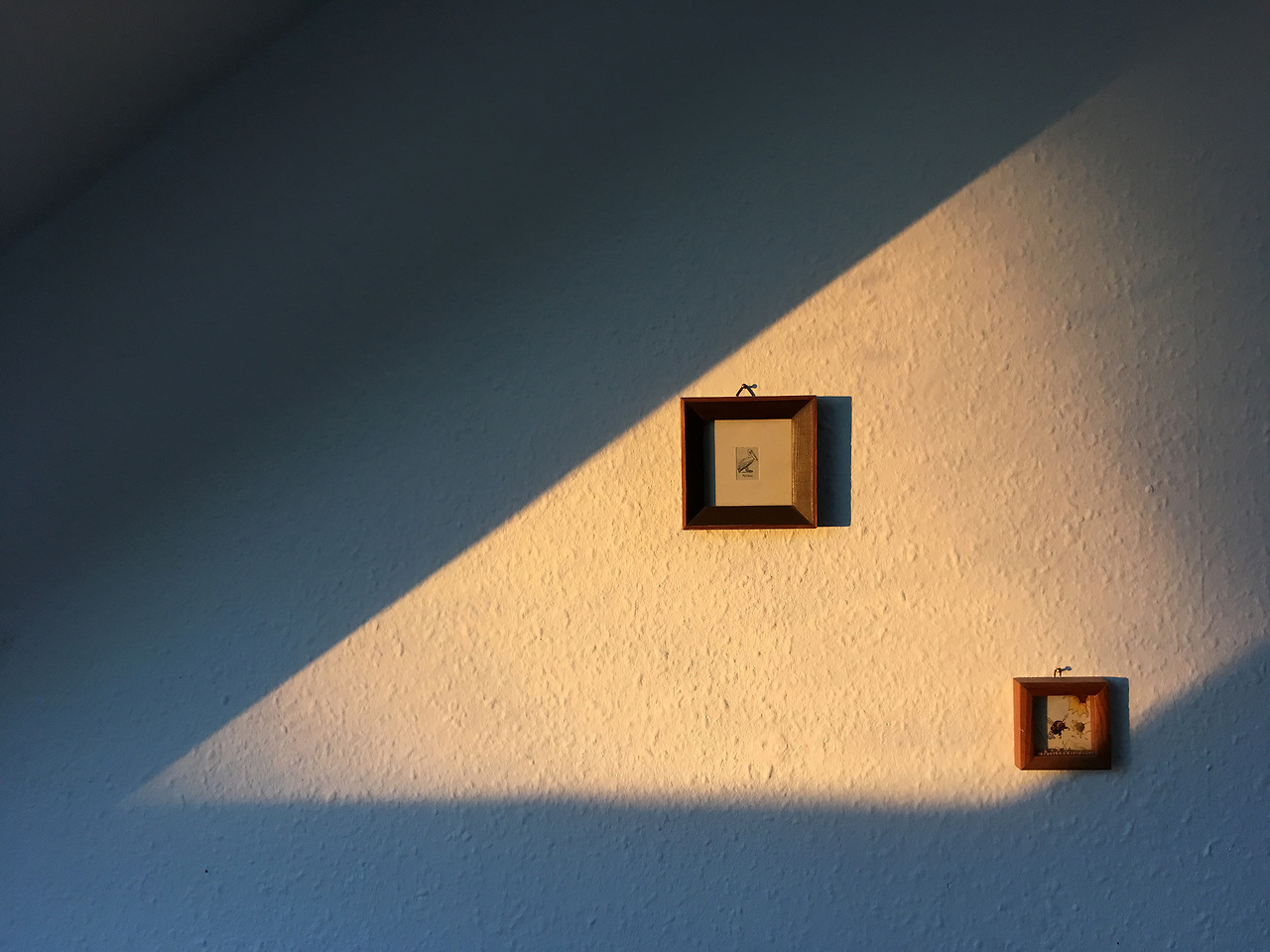 A color photograph of two picture frames on a white wall with sunlight on them.