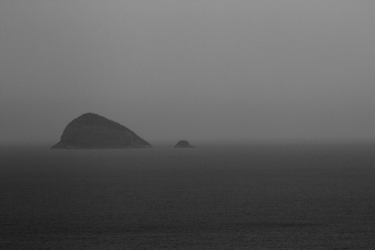 A grainy black and white photograph of a mountain in the middle of the ocean.