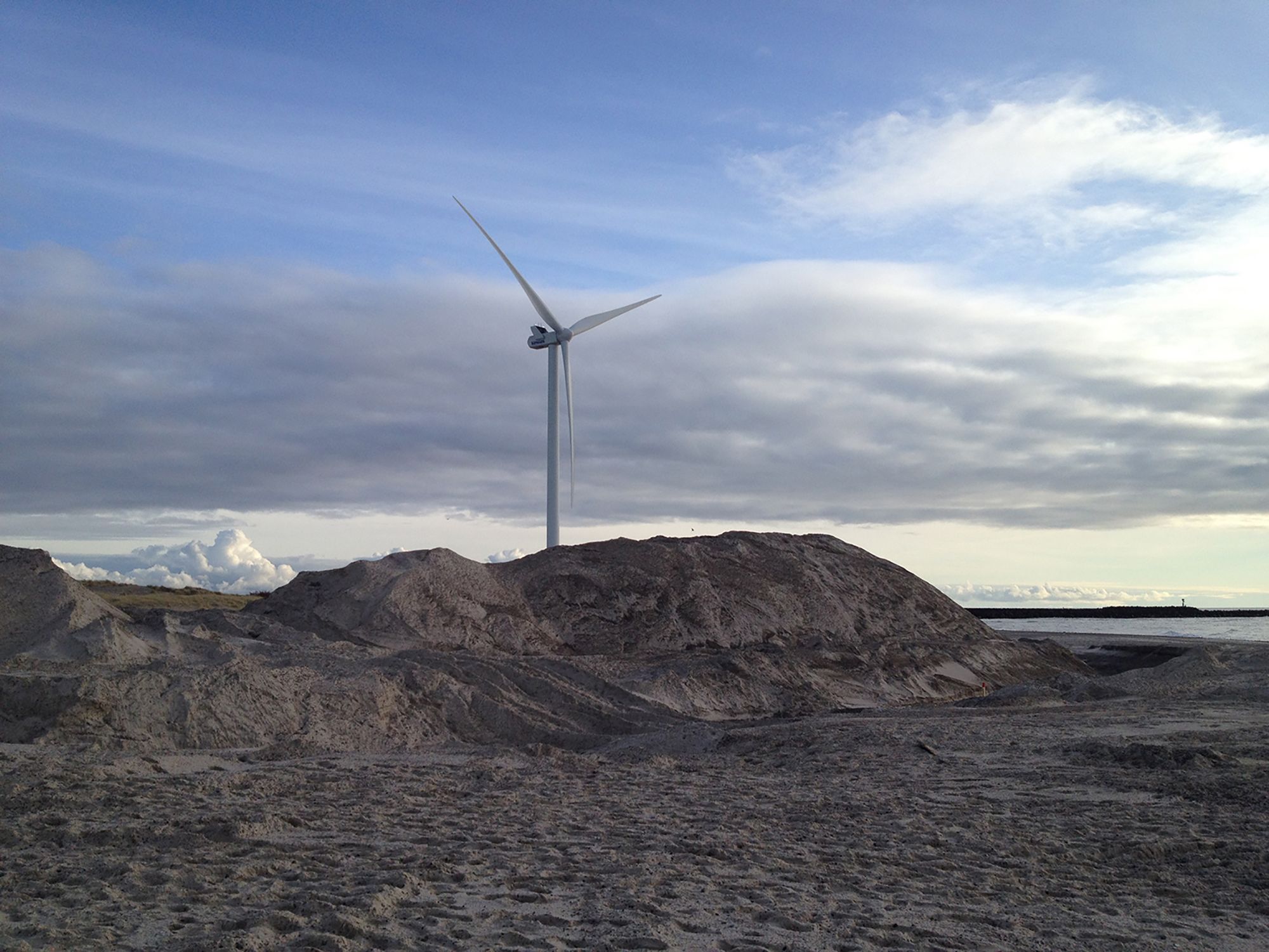 A color photograph of a wind turbine on the beach.