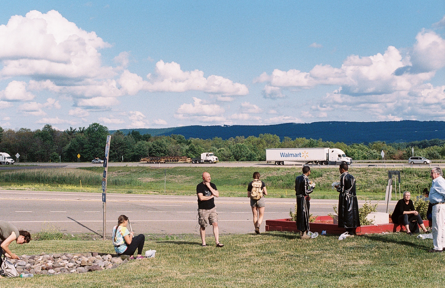 A color photograph of people standing by a roadside.