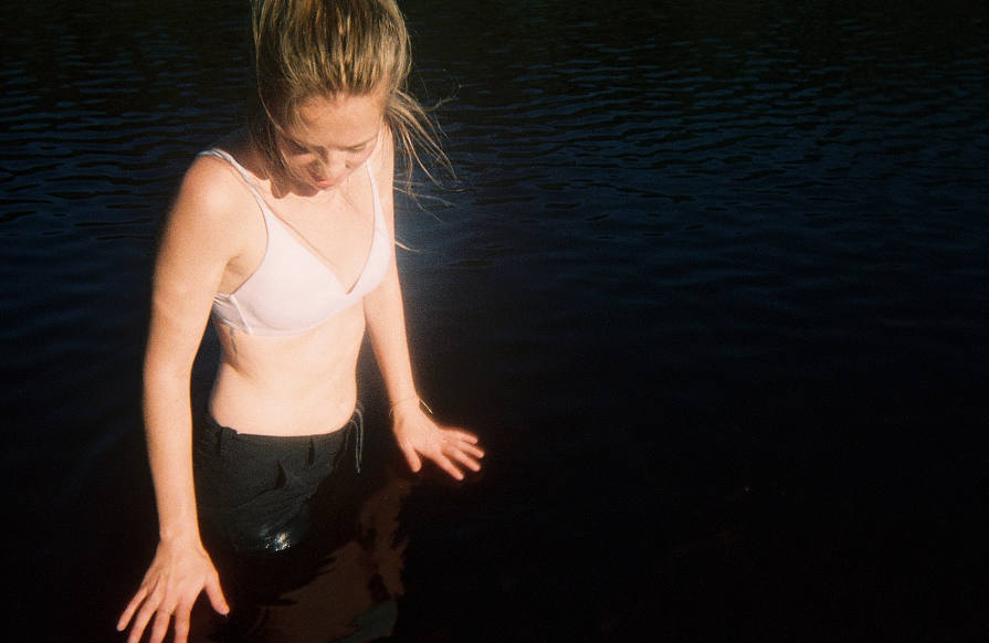 A color photograph of a girl standing in a lake.